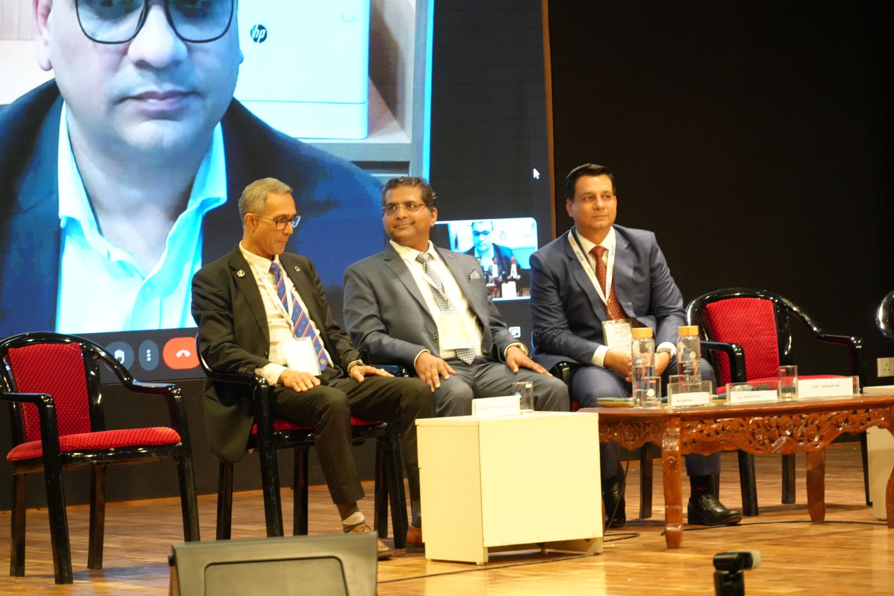 Panellists seated on stage during a session with a remote speaker on screen